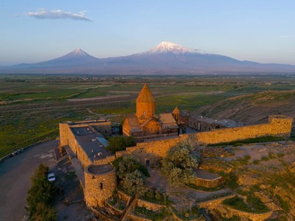 Historic monastery with surrounding wall and view of Mount Ararat at sunrise, aerial view, Chor