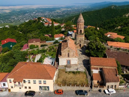 Village view with church tower and brick buildings, surrounded by green hills and wide landscape,