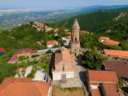 Historic church with tower in a village surrounded by mountains with red tiled roofs, aerial view,