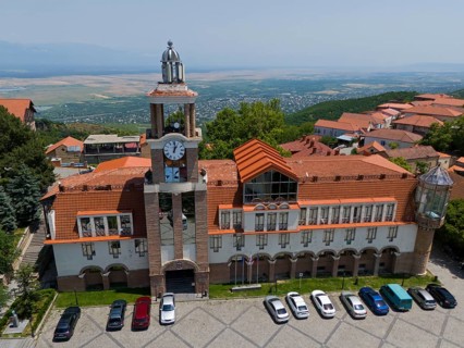 Large building with clock tower and surrounding traditional roofs on a slope, aerial view, town