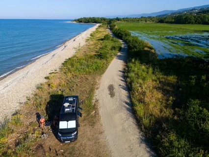 A van parked on a beach along a coastal road with lush vegetation and sea view, aerial view,
