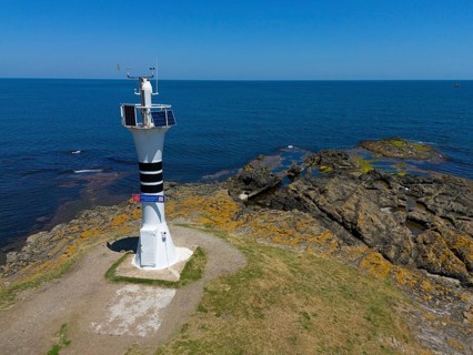Close-up of a lighthouse on a rocky coast with the wide sea and blue sky, aerial view, Yason Burnu