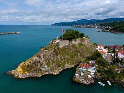 Castle on a rock formation near coastal houses and mountains with clouds, aerial view, fortress,