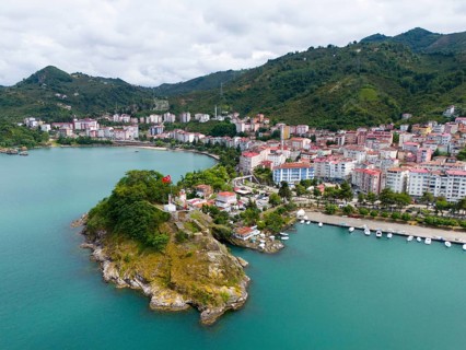 Coastal town with mountains and green hill, Turkish flag on a small cape, aerial view, fortress,