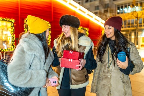 Three cheerful young women holding christmas gifts and enjoying a winter night out in a decorated