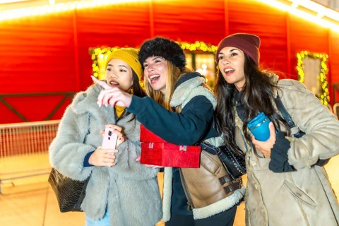 Three young women holding christmas gifts and a smartphone are enjoying the christmas spirit,