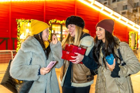 Three cheerful young women holding christmas gifts, enjoying christmas market at night, winter