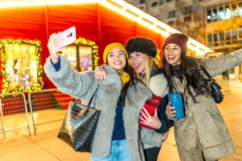 Three happy female friends taking a selfie at a christmas market, enjoying the festive atmosphere