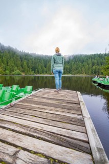 Woman standing alone on a wooden jetty in front of a quiet lake surrounded by forest, Mummelsee,