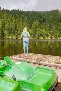 A person stands on a footbridge, looking at a quiet lake in the forest, Mummelsee, Seebach, Ortenau