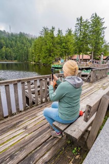 Woman taking a photo of the lake while sitting on a wooden bench surrounded by forest, Mummelsee,