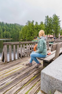 A woman sits relaxed on a wooden bench overlooking the tranquil lake and forest, Mummelsee,