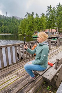 Woman sitting on a wooden footbridge and holding a camera over a lake, Mummelsee, Seebach, Ortenau