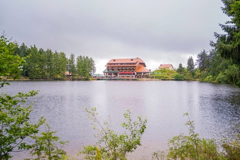A hotel on the shore of a lake, surrounded by forest and overcast skies, Mummelsee, Seebach,