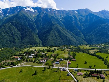 A small village in the middle of a vast green landscape with high mountains in the background,