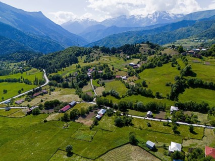 Hilly landscape with small settlements and green fields surrounded by mountains, aerial view,