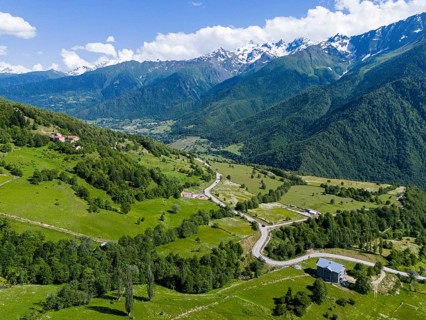 Panoramic view of a valley with roads and forests, surrounded by mountains under a clear sky,