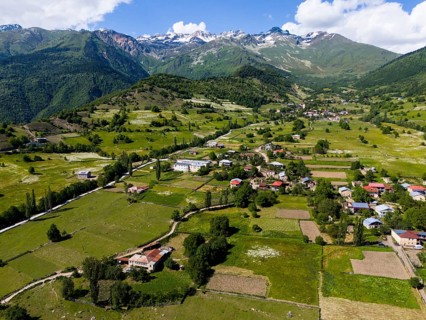 Mountain landscape with scattered villages and green meadows under a blue sky with clouds, aerial