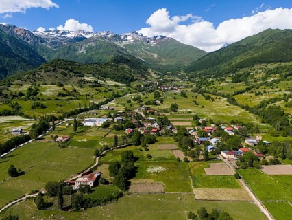Vast landscape with villages and fields under a blue sky, framed by mountains, aerial view,