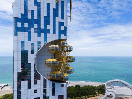 Modern building with futuristic design and golden gondolas on the coast with sea background, aerial
