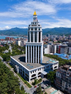 A tall modern building in an urban environment with mountains, aerial view, Sheraton Hotel, Batumi,