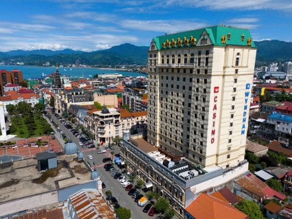 Large hotel building in a coastal town with mountains in the background and lively street scene,