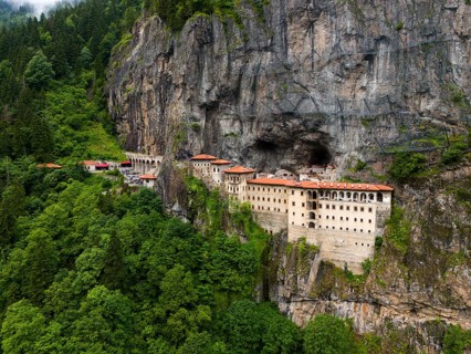 A monastery embedded in a green rocky landscape surrounded by dense forest, aerial view, Sumela