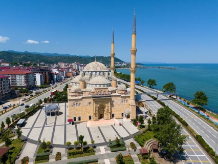 Panoramic view of a large mosque with minarets on a coastline flanked by streets and buildings,