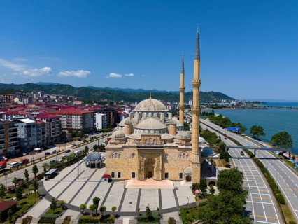 Large mosque with several minarets on the coast, surrounded by modern buildings and mountains in