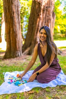 Latin mother arranging colorful baby toys on a blanket in a park, enjoying a sunny day outdoors