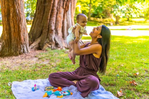 Latin mother joyfully lifting her baby daughter while sitting on a blanket in a park, enjoying