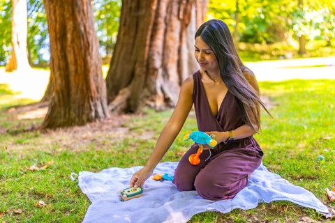 Latin mom arranging colorful baby toys on blanket in park, enjoying quality time with her child in