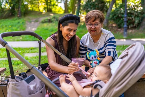 Grandmother, mother and baby girl enjoying time together at the park, feeding the baby girl and