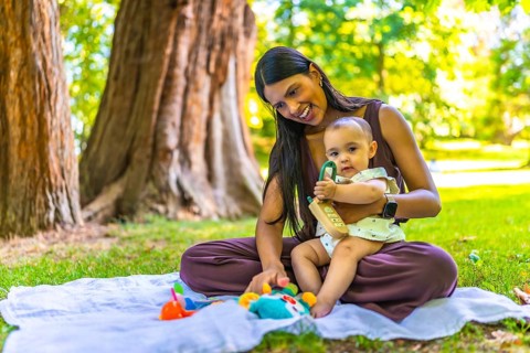 Latin mother and her baby daughter enjoying playtime with colorful toys on a blanket, under the