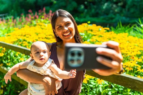 Happy latin mother holding her baby daughter, taking a selfie with a smartphone in a garden full of
