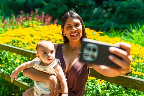 Happy latin mother holding her baby daughter and taking a selfie with smartphone in a beautiful