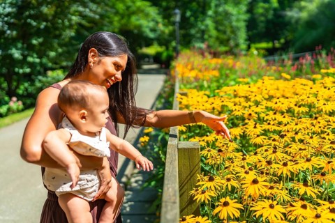 Latin mother holding her baby daughter and showing her yellow flowers in bloom in a sunny botanical