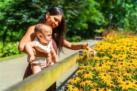 Latin mother holding her baby daughter and showing her yellow flowers in a park during a sunny day
