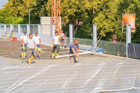 Group of construction workers on a building site with warning signs and a crane nearby, car park