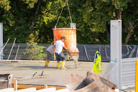 Construction workers pouring concrete from a concrete mixer on a building site with lattice fence