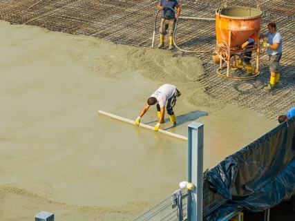 Workers smoothing concrete on a construction site while a concrete mixer stands in the background,