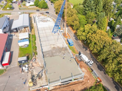 Aerial view of a construction site with crane and concrete foundation, surrounded by trees in