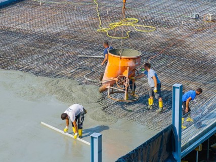 Workers pouring concrete on a construction site with concrete mixer and steel frame structure in