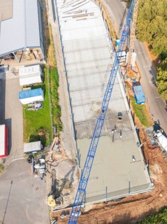 Aerial view of a construction site with blue crane and concrete surface next to a road, car park