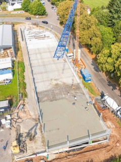 Top view of a construction site with crane and workers, surrounded by trees and roads, car park