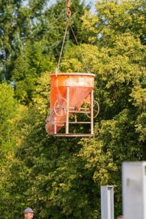 Concrete mixer being lifted with a crane on a construction site near trees, car park construction,