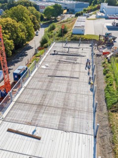 Workers on construction site with crane in sunny weather, surrounded by roads and fences, car park