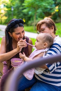 Mother feeding her baby a meal in the park, with grandmother holding the child, enjoying family