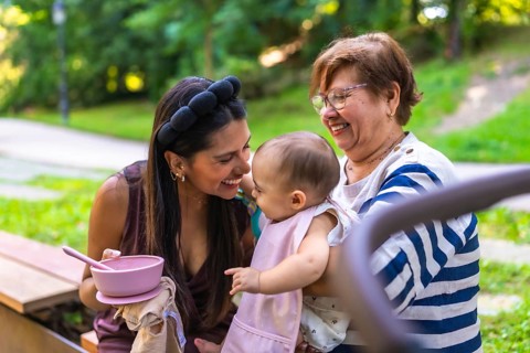 Grandmother holding her granddaughter while mother is feeding her in a park, enjoying family time