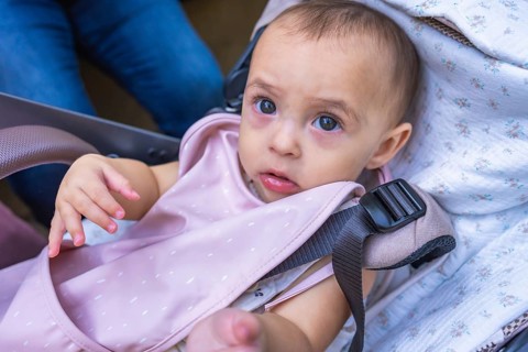 Adorable baby girl sitting in a stroller, secured with a safety harness and wearing a pink bib